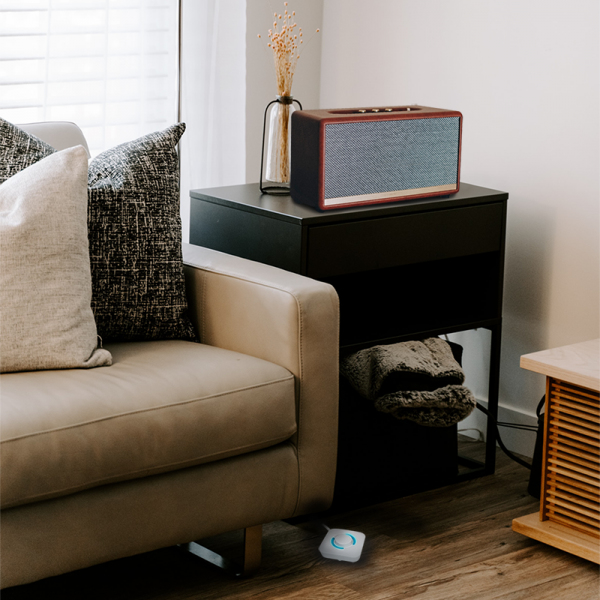 Une enceinte Bluetooth en bois est posée sur une table noire à côté d'un canapé beige avec des coussins.