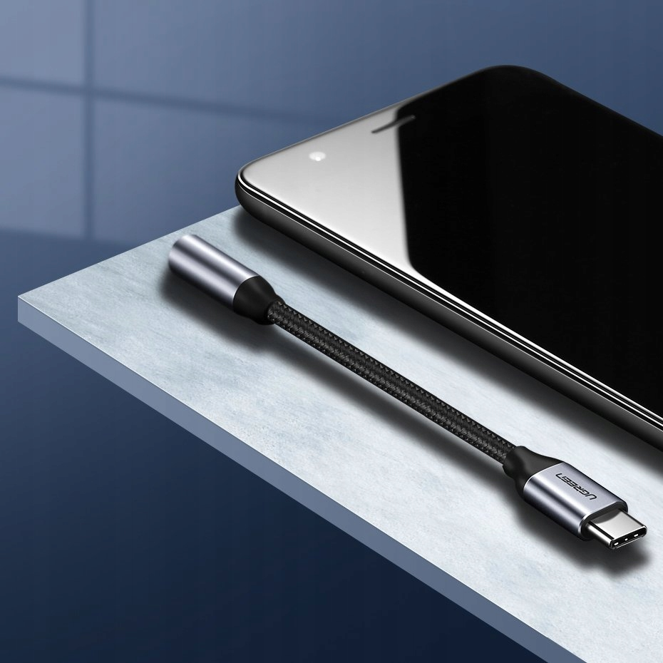 Kabel adaptera typu C leży na niebieskiej powierzchni obok smartfona.