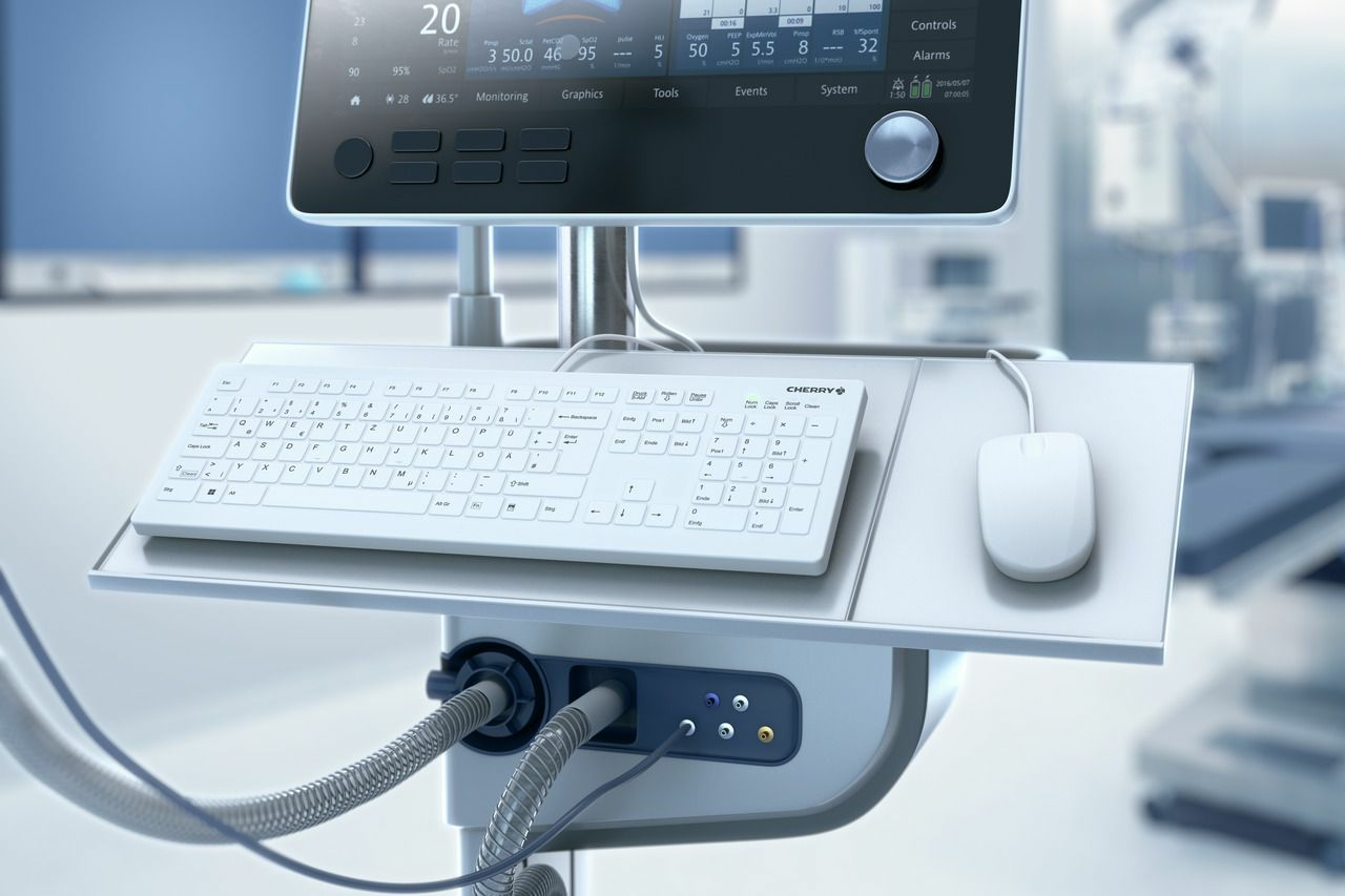 Medizinisches Gerät mit Monitor, weißer Tastatur und Maus auf einem Ständer in einem hellen Raum.