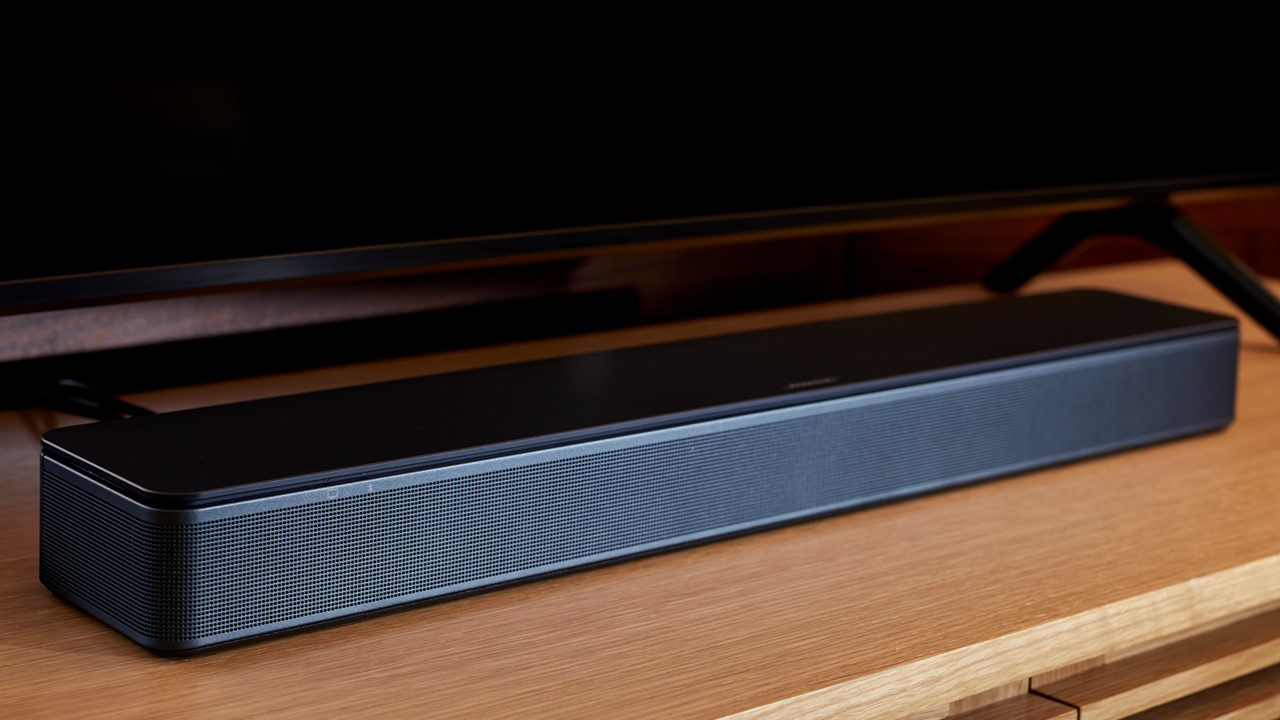 Una barra de sonido negra sobre un mueble de madera bajo un televisor.