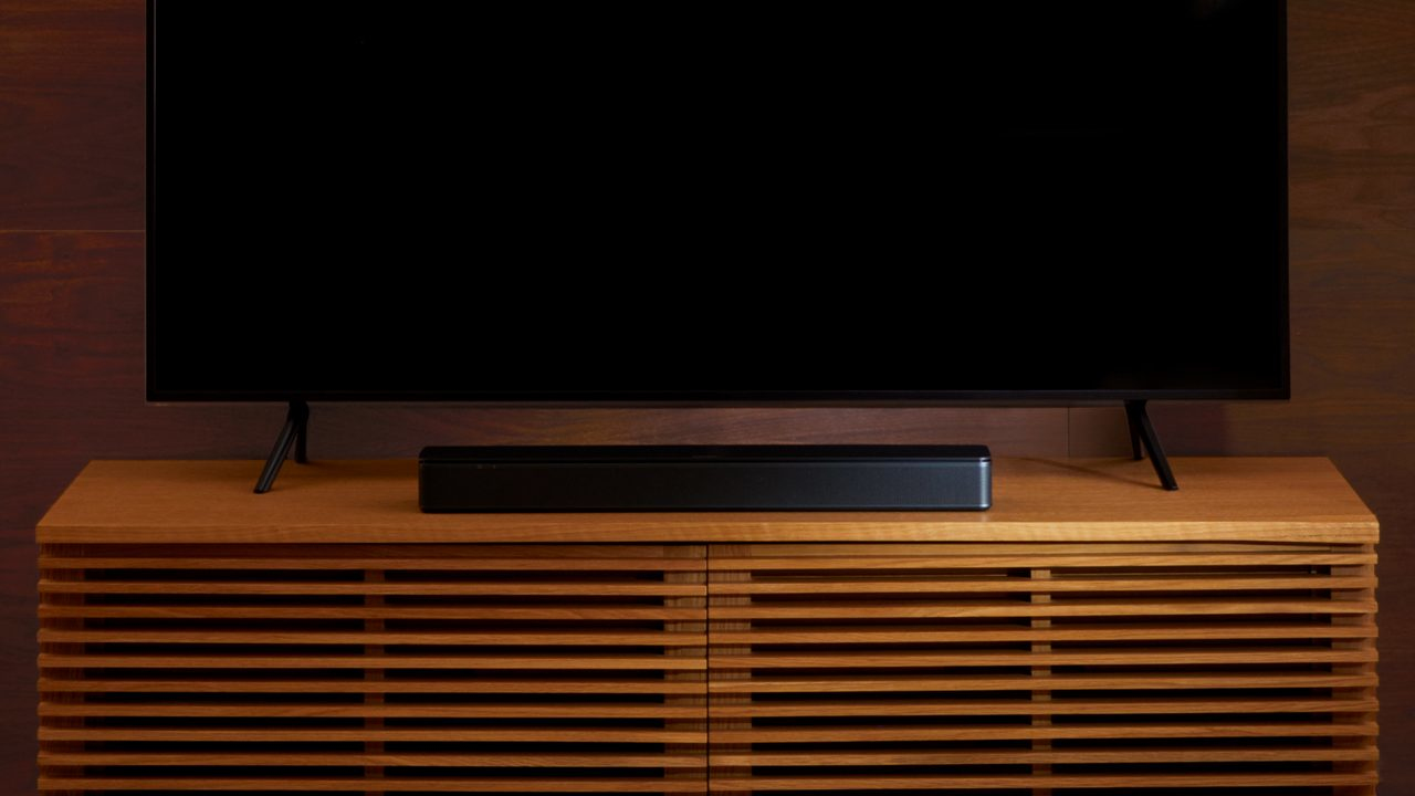 Un televisor negro y una barra de sonido sobre un mueble de madera ante una pared oscura.