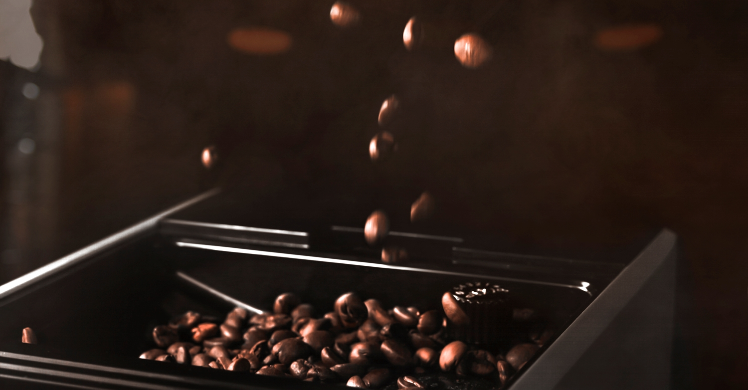 Chicchi di caffè cadono nel contenitore di una macchina da caffè su sfondo scuro.