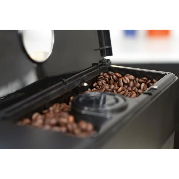 An open black coffee machine hopper filled with roasted brown coffee beans against a blurred background.