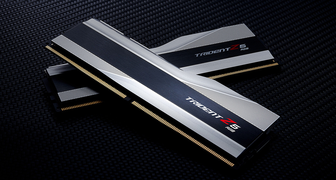 Dwie kości RAM Trident Z5 RGB ze srebrno-czarnymi radiatorami leżą ukośnie na ciemnej powierzchni.