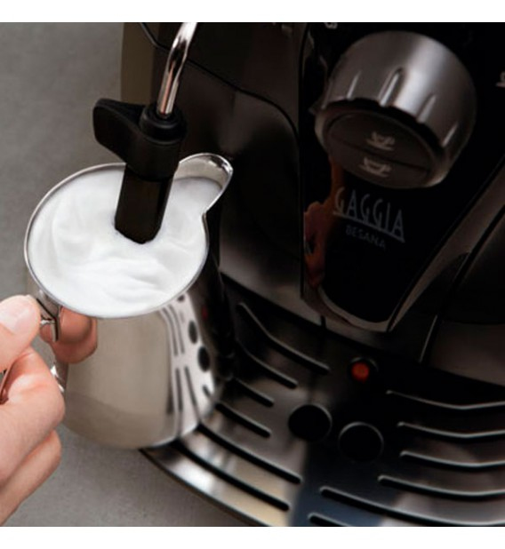 Una mano sostiene una jarra mientras una cafetera Gaggia espuma leche con su vaporizador.