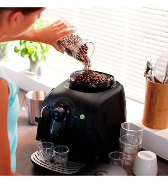 Una mujer vierte granos de café de un frasco en una cafetera negra.