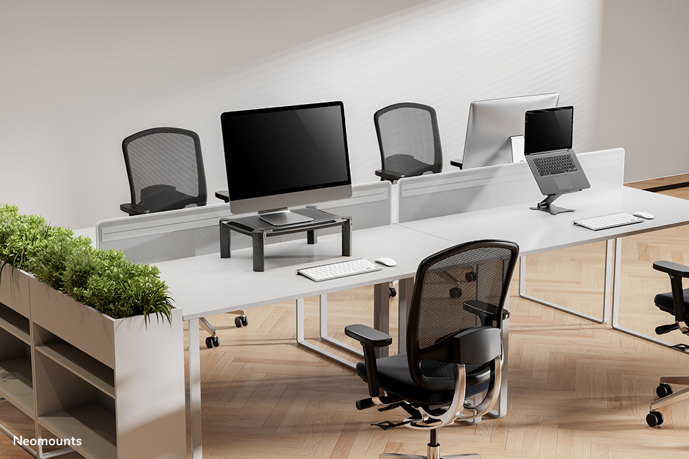 Modern office desks with computers, laptops, keyboards, and ergonomic chairs on hardwood flooring.