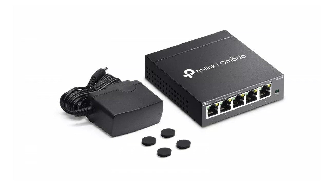 Beyaz arka planda güç adaptörü ve dört küçük kauçuk ayağa sahip siyah bir Tp-Link Omada ağ anahtarı.