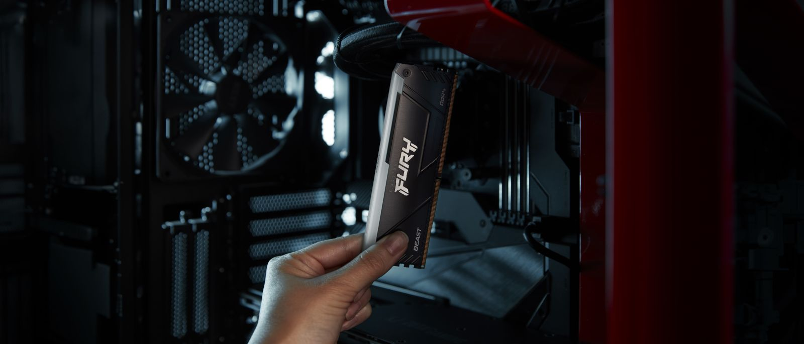 Eine Hand hält einen Kingston FURY Beast RAM-Riegel vor ein PC-Gehäuse mit Lüfter.