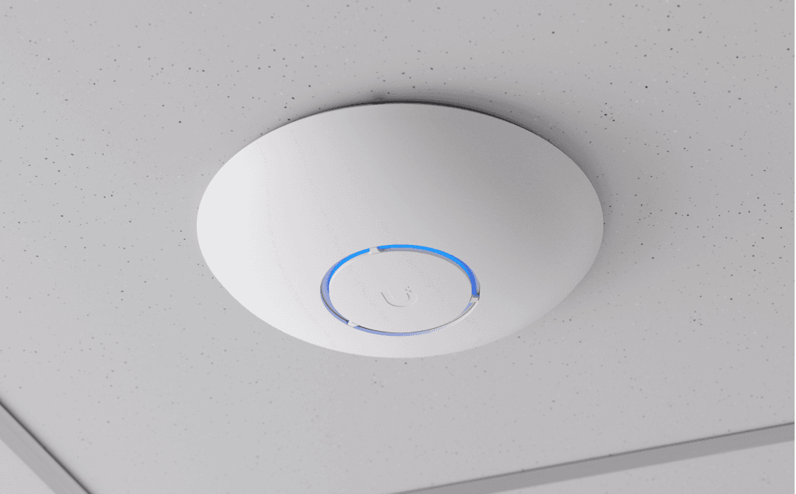 Biały, okrągły punkt dostępowy Wi-Fi z świecącym niebieskim pierścieniem jest zamontowany na nakrapianym suficie.