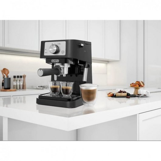 Macchina da caffè nera su bancone bianco con due bicchierini e una tazza grande di cappuccino davanti.