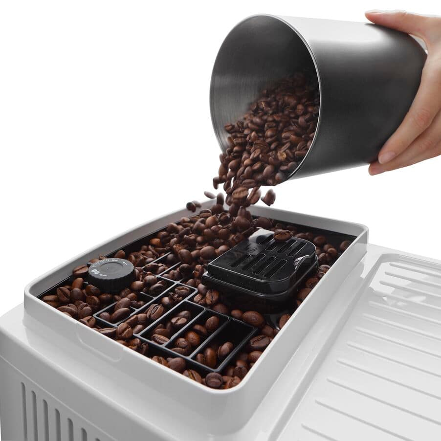 Kaffeebohnen werden aus einem dunklen Behälter in das Mahlwerk einer weißen Kaffeemaschine gefüllt.