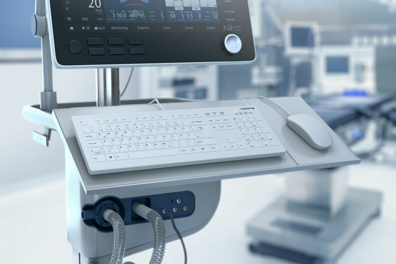 Medizinischer Monitor mit weißer Tastatur und Maus auf einer Ablage in einem Krankenhaus.