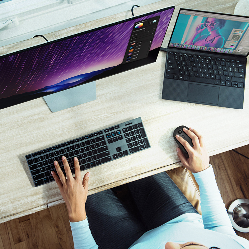 Persona trabajando en un escritorio con un monitor ultra ancho, portátil, teclado y ratón.
