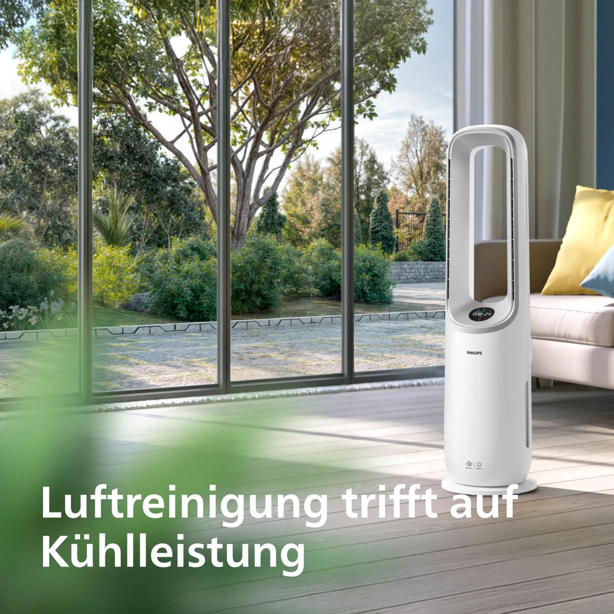 Ein weißer Turmventilator steht in einem hellen Wohnzimmer vor großen Fenstern mit Gartenblick.