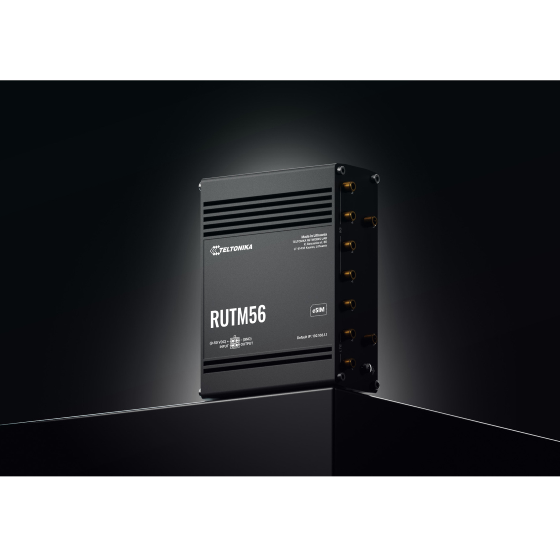 A black Teltonika RUTM56 router stands on a dark surface against a neutral background.
