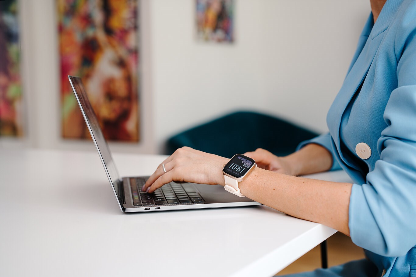 Kobieta w niebieskiej marynarce pisze na laptopie ze smartwatchem przy białym biurku.