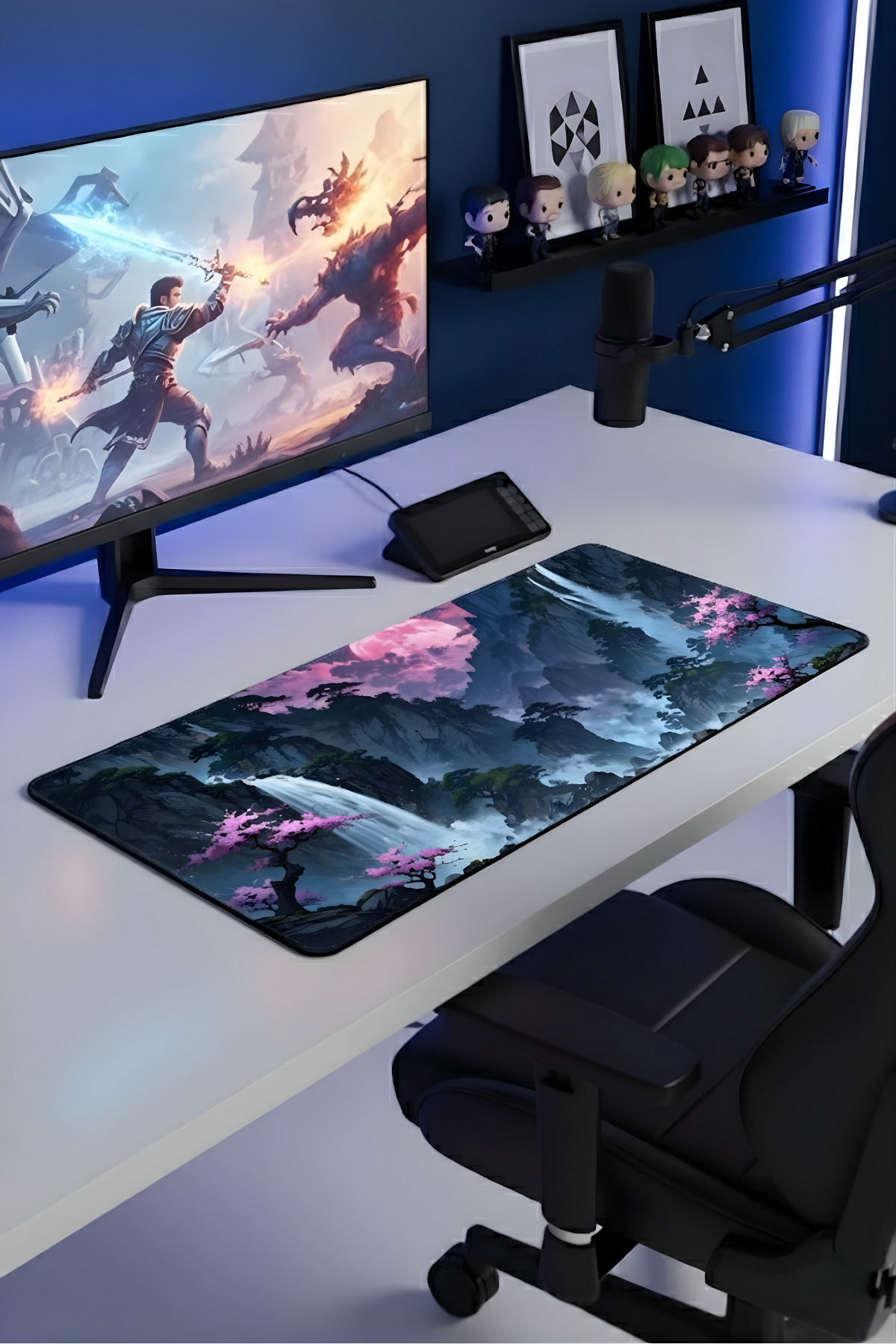 Monitör, büyük mouse pad ve rafta figürler bulunan bir oyuncu masası.