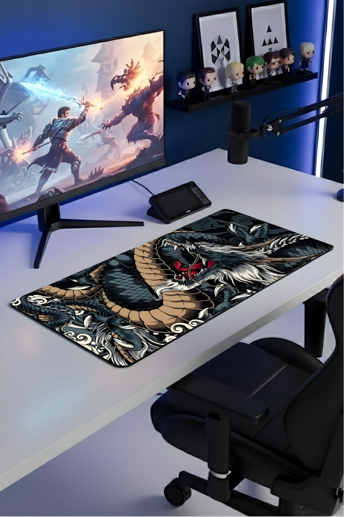 Monitör, ejderha mouse pad, mikrofon ve figürlerin olduğu oyuncu masası.