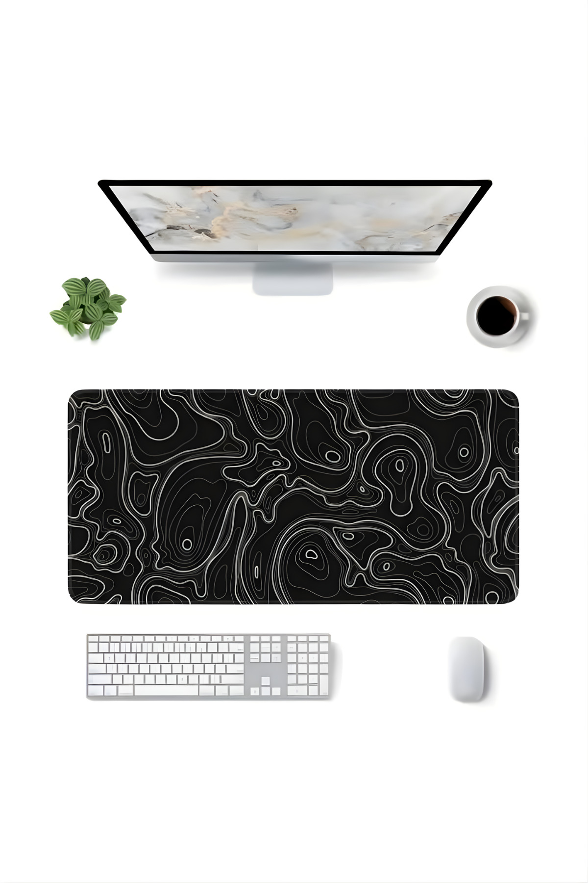 Monitör, klavye, fare, topografik desenli mousepad, bitki ve kahve olan bir masanın üstten görünümü.