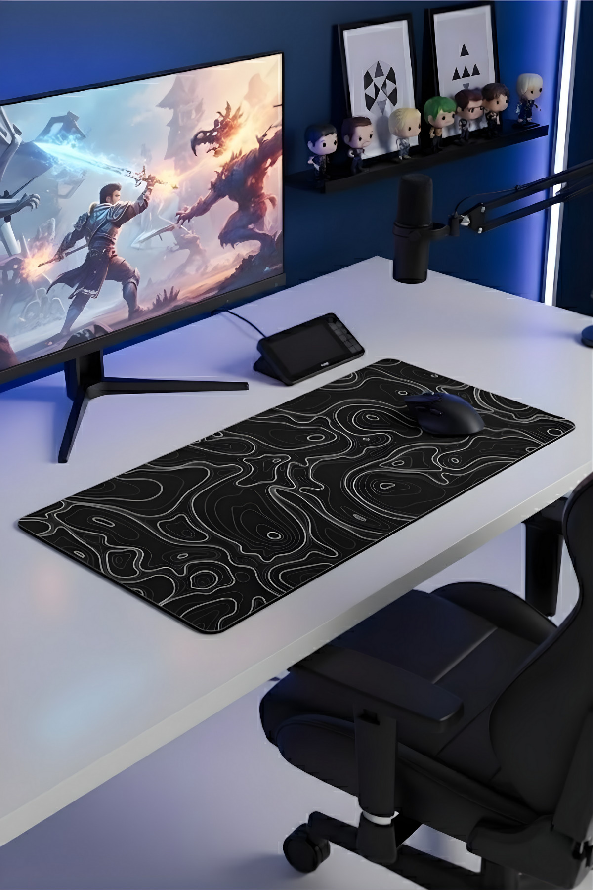Mavi aydınlatmalı duvar önünde monitör, büyük siyah mousepad, fare ve figür rafı bulunan modern oyun masası.