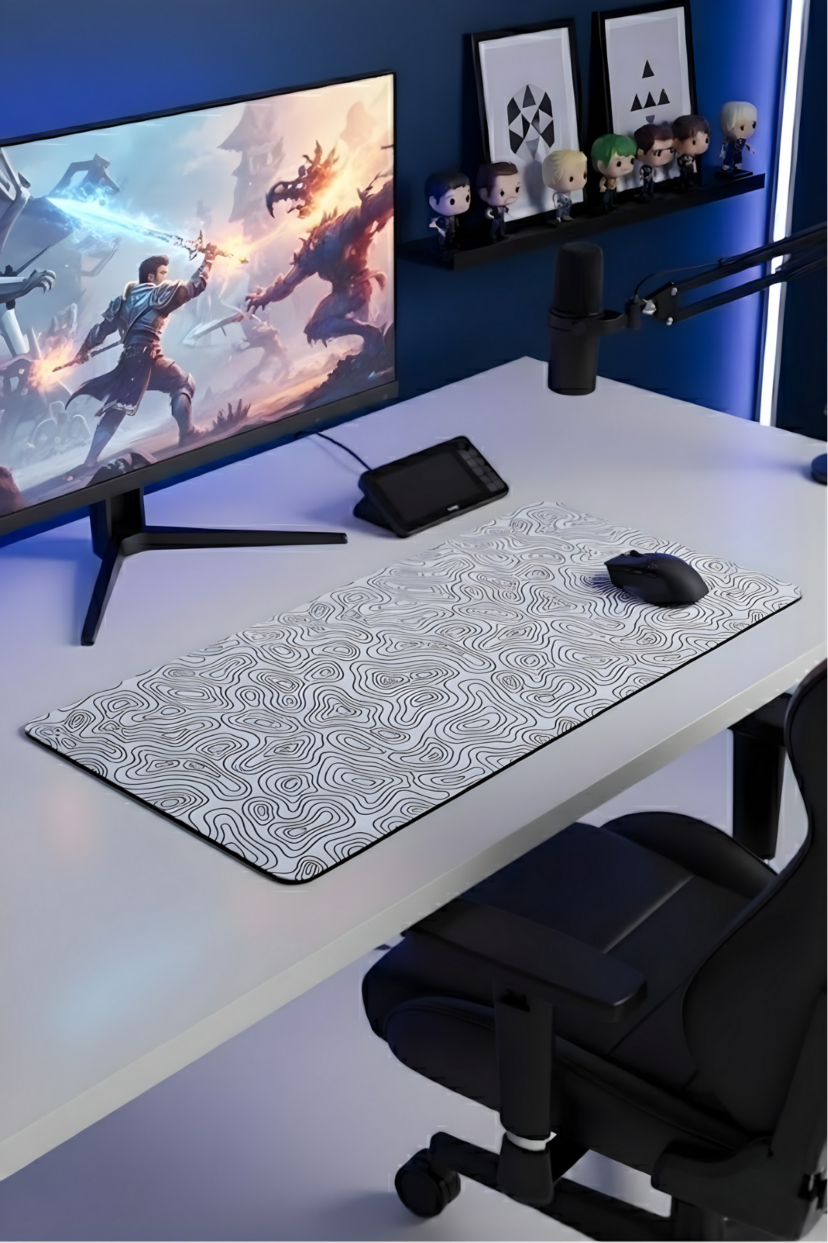 Fantezi savaş sahnesi gösteren monitör, topoğrafik desenli mousepad ve siyah sandalyeli bir oyuncu masası.