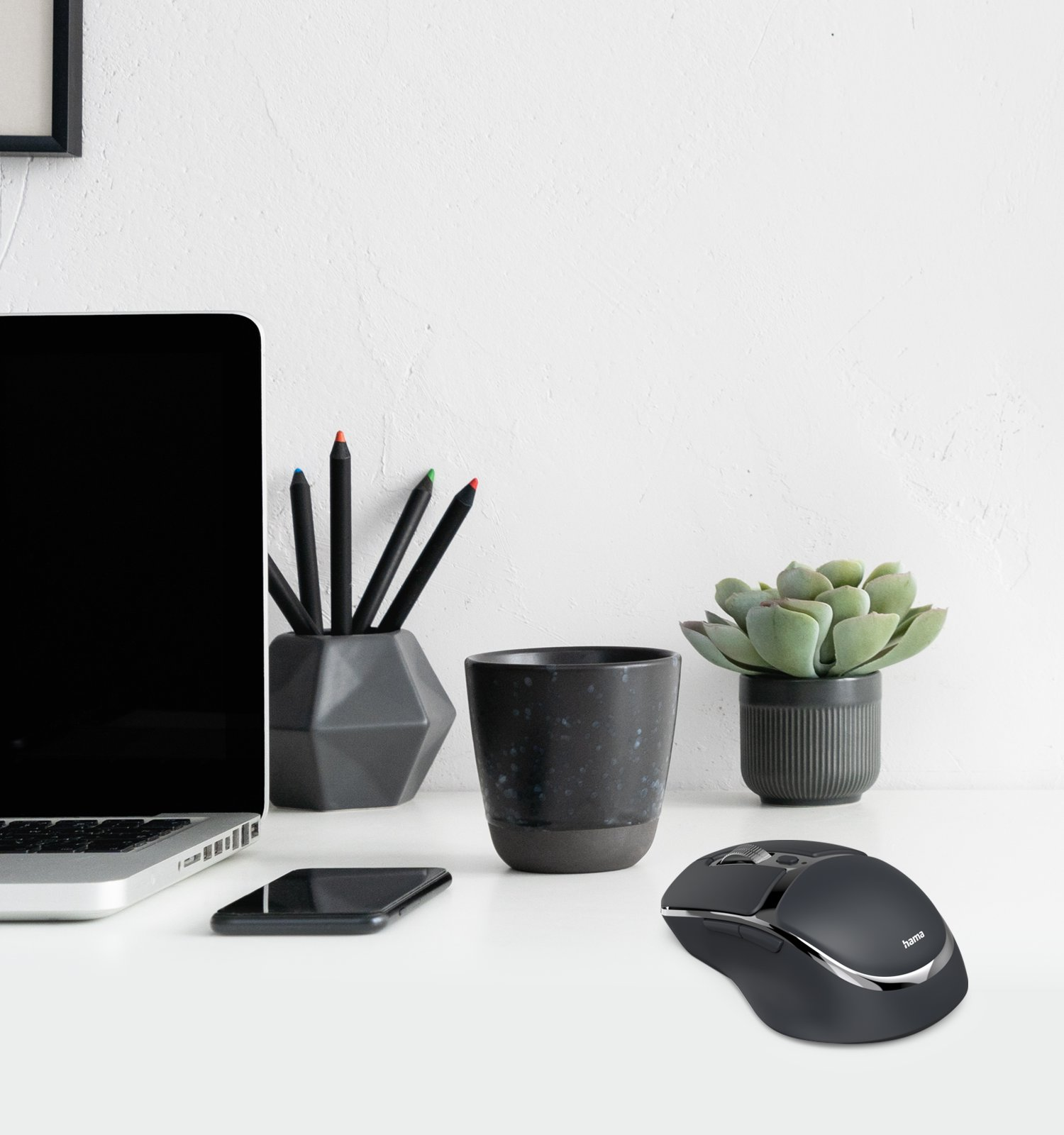 Ein minimalistischer Schreibtisch mit Laptop, schwarzer Maus, Kaffeetasse, Stiften und einer Sukkulente.