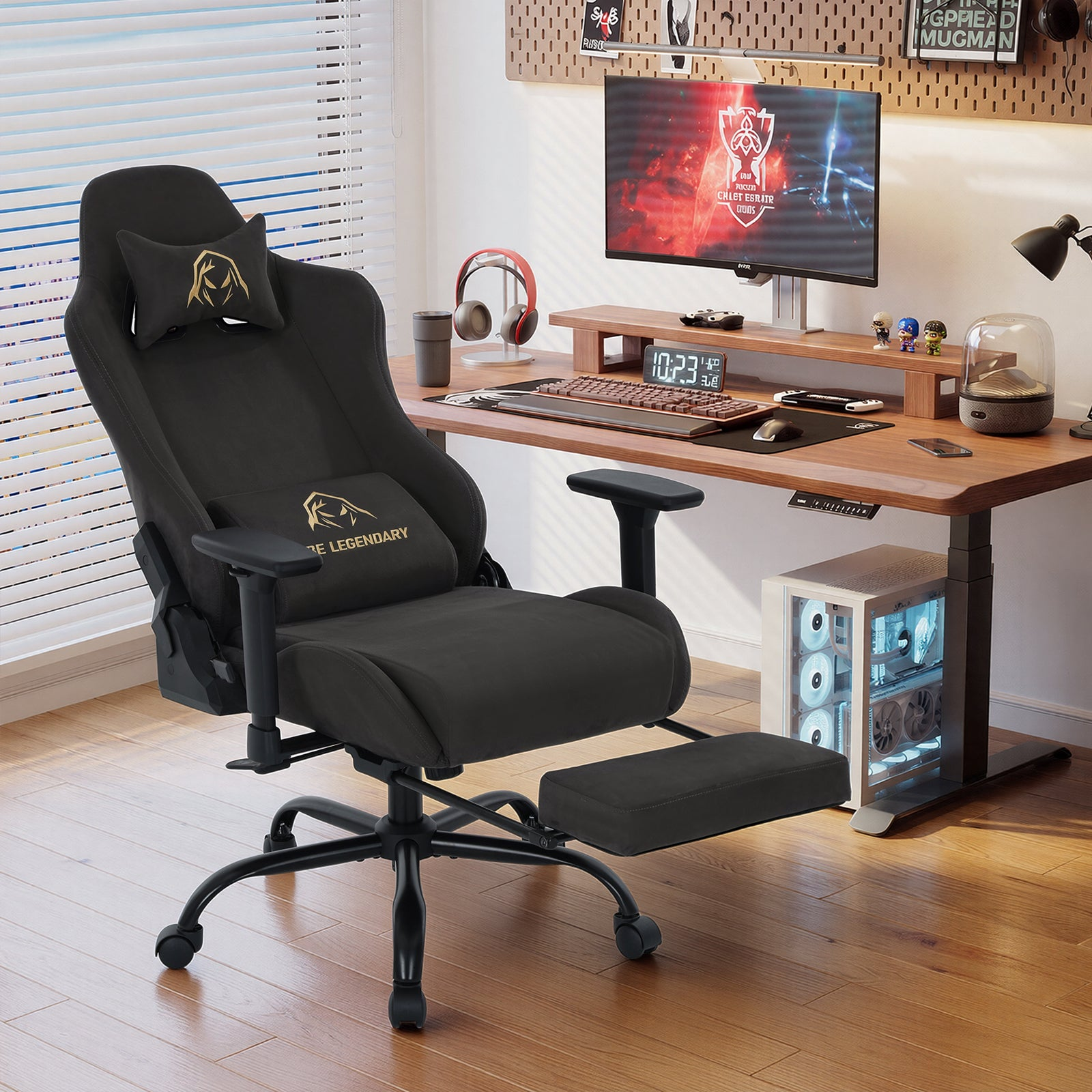 Ein schwarzer Gaming-Stuhl mit Fußstütze steht vor einem Holztisch mit PC und Monitor in einem hellen Zimmer.