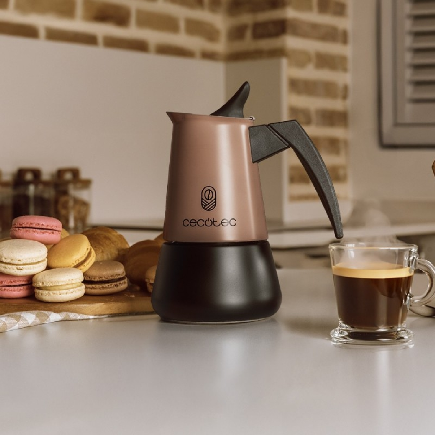 Una moka Cecotec color moca e nero su un bancone accanto a una tazza di caffè fumante e ai macaron.