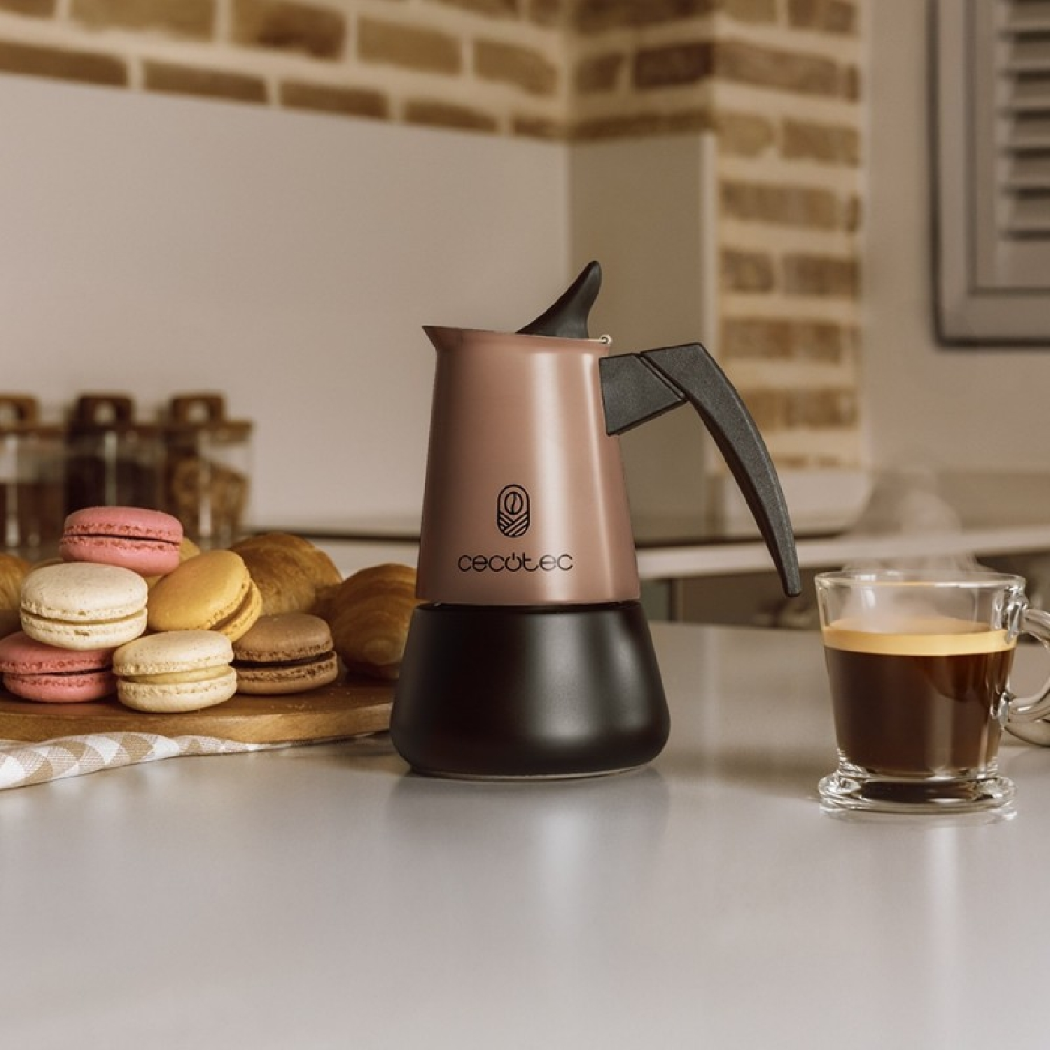 Una cafetera italiana en la encimera junto a una taza de café caliente y macarons.