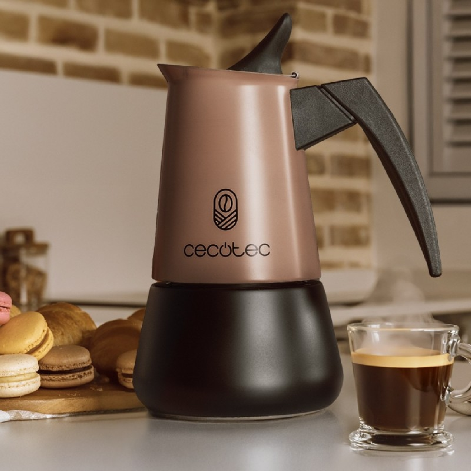 Una moka oro rosa e nera su un bancone accanto a un bicchiere di espresso fumante e dolci.