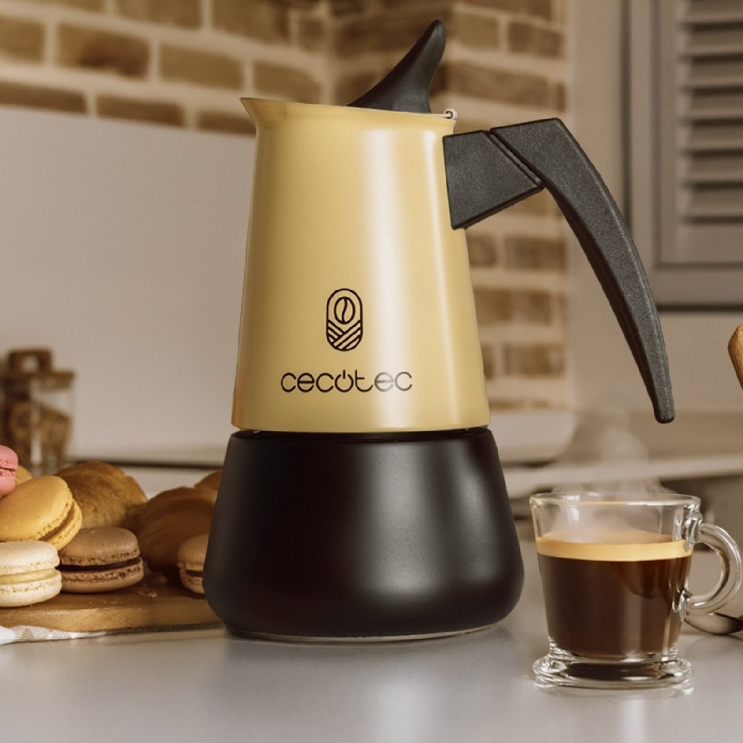 Una cafetera italiana Cecotec en tonos beige y negro junto a una taza humeante de café y pasteles.