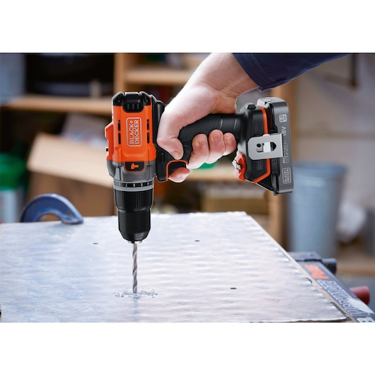 Eine Hand hält einen orange-schwarzen Akkubohrschrauber von Black and Decker beim Bohren in ein Metallblech.