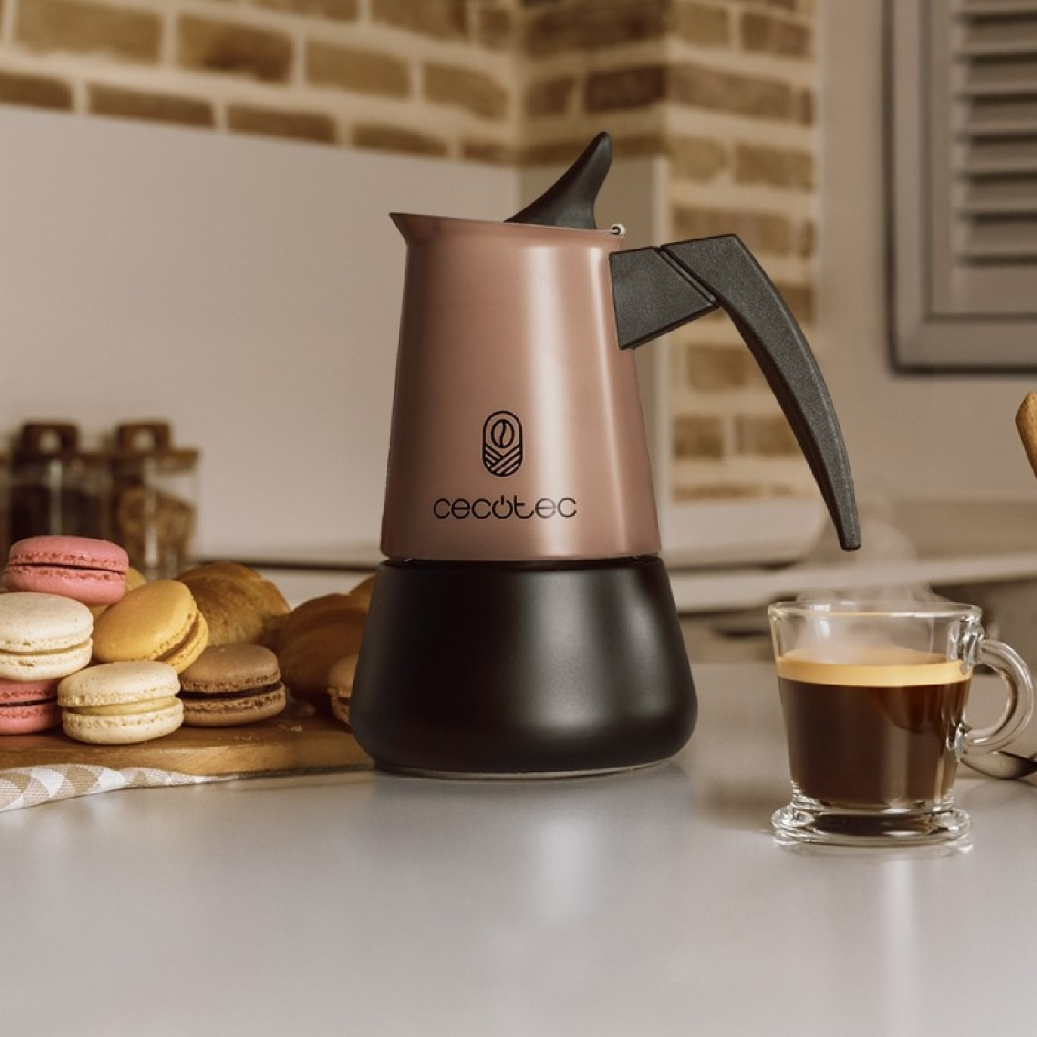 Una caffettiera Cecotec rosa e nera su un piano cucina con una tazza di caffè e macaron.