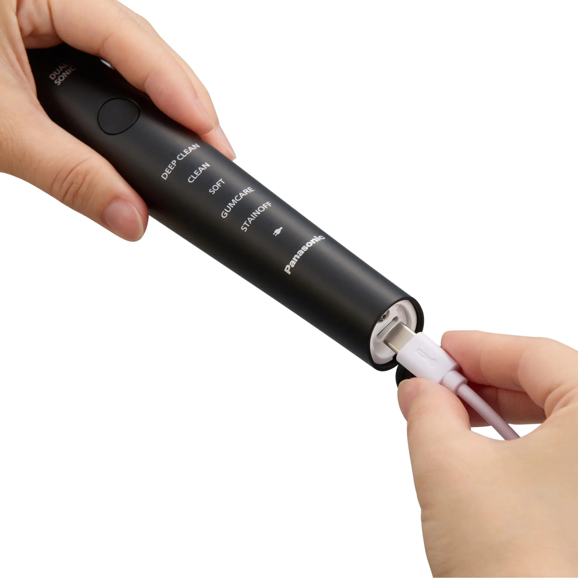 Ręce trzymają czarną szczoteczkę Panasonic, podłączając biały kabel ładujący USB-C.