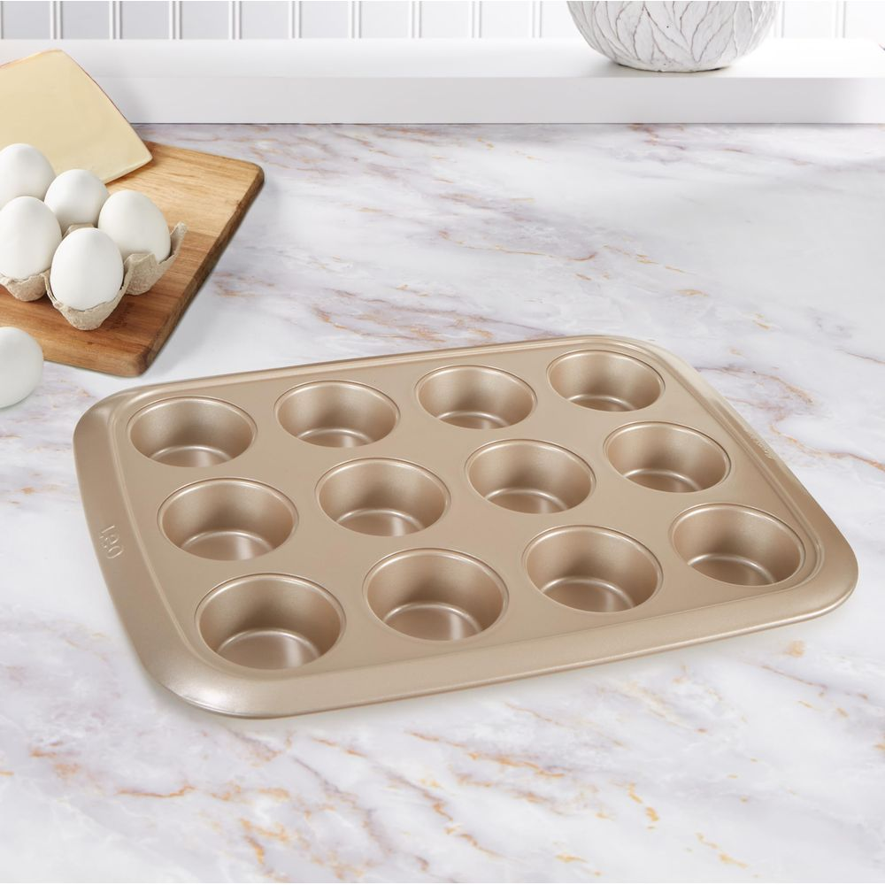 Złota forma do muffinek na marmurowym blacie, po lewej stronie jajka na desce.