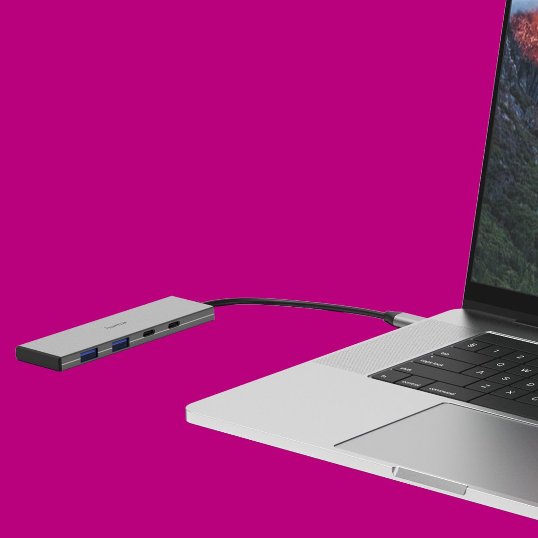 Srebrny hub USB-C podłączony do laptopa na żywym magenta tle.