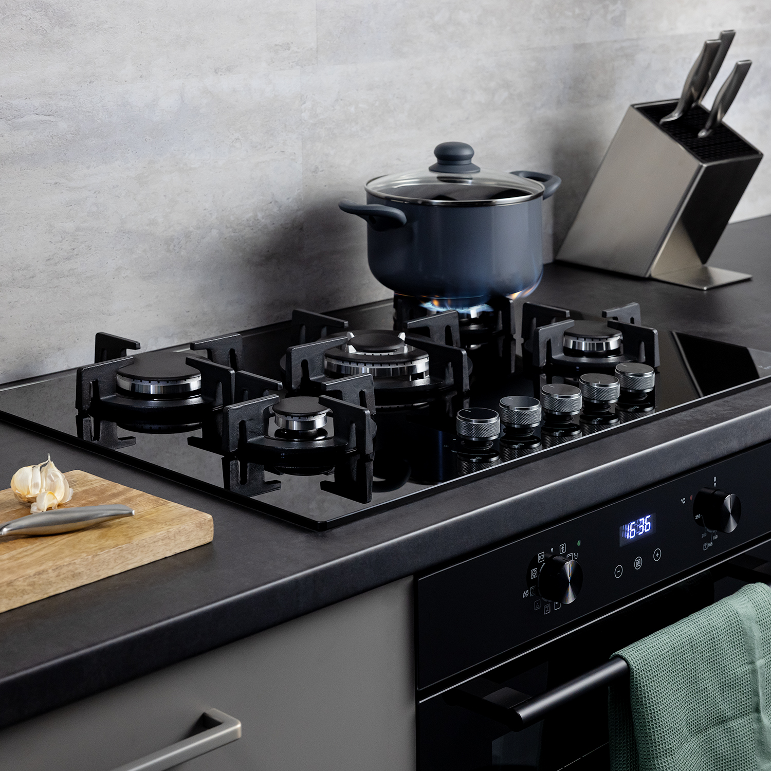 Moderno piano cottura a gas nero su piano di lavoro scuro con pentola e tagliere.