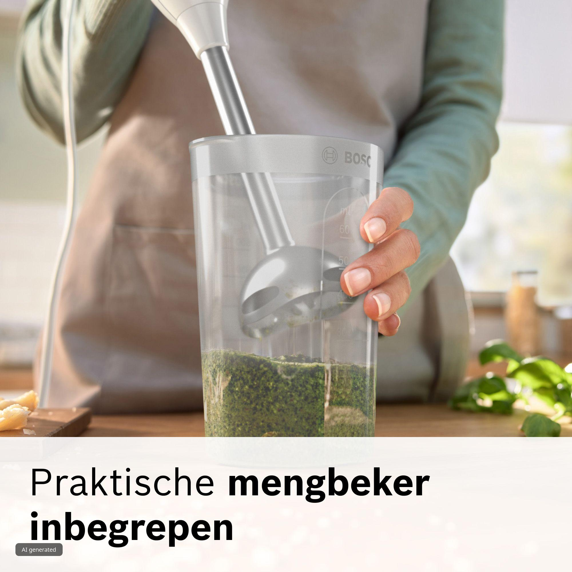 Une personne utilise un mixeur plongeant dans un grand gobelet pour mixer des herbes.
