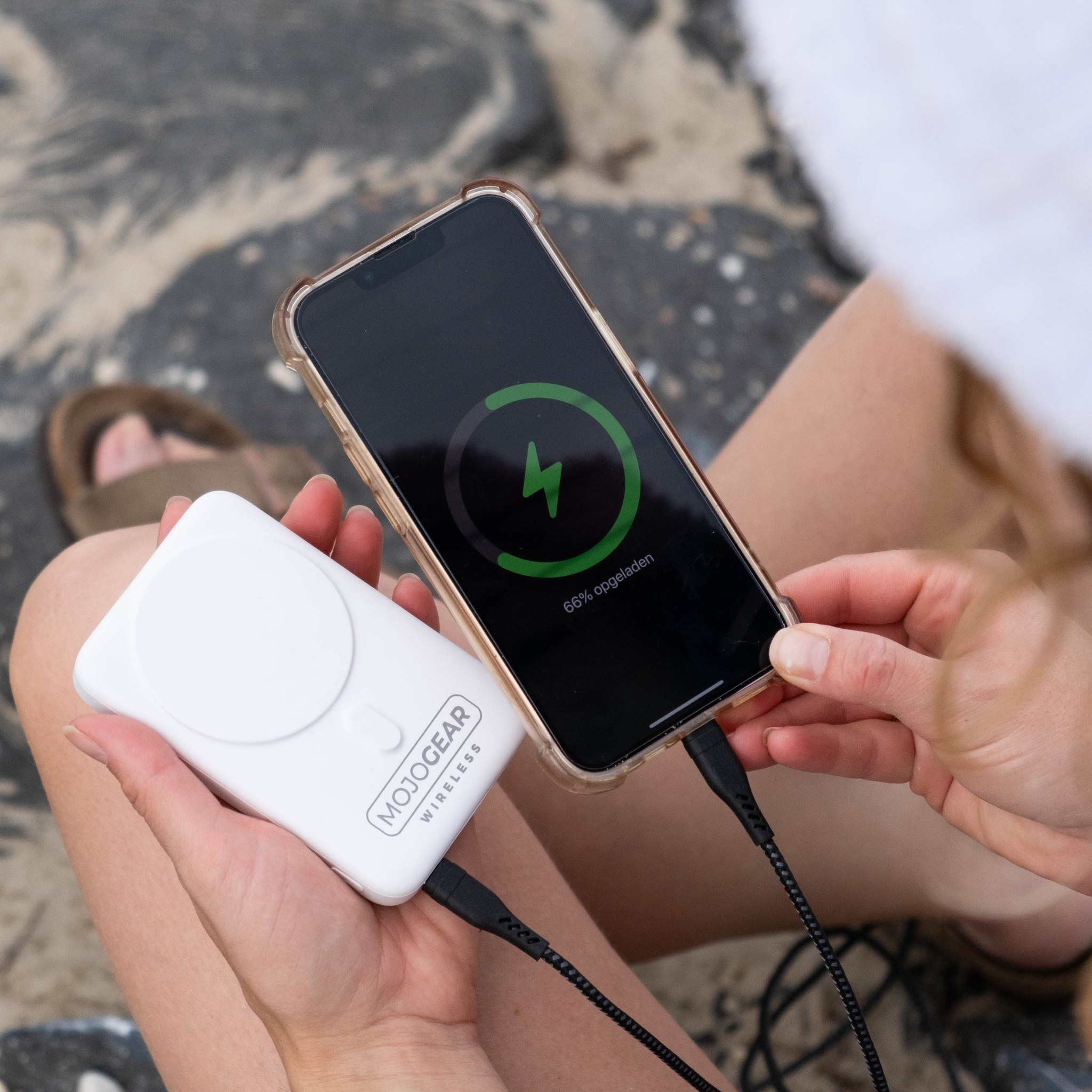 Une personne tient une batterie externe blanche MojoGear et un smartphone en charge.