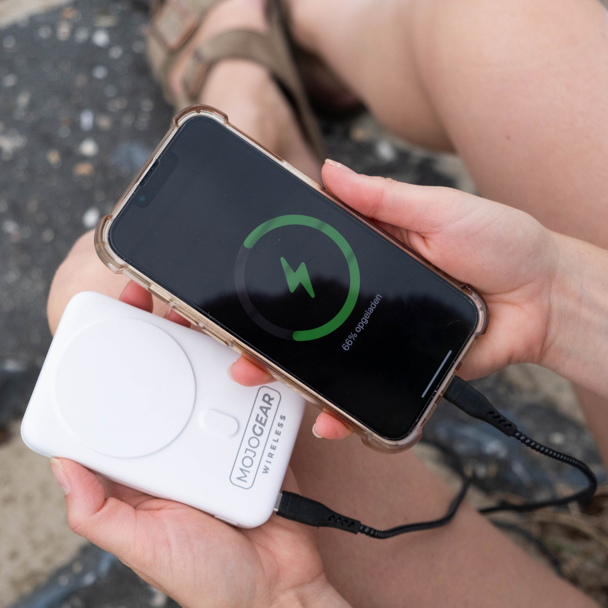 Personne tenant un smartphone affichant 66 pour cent de batterie et une power bank sans fil Mojo Gear blanche.