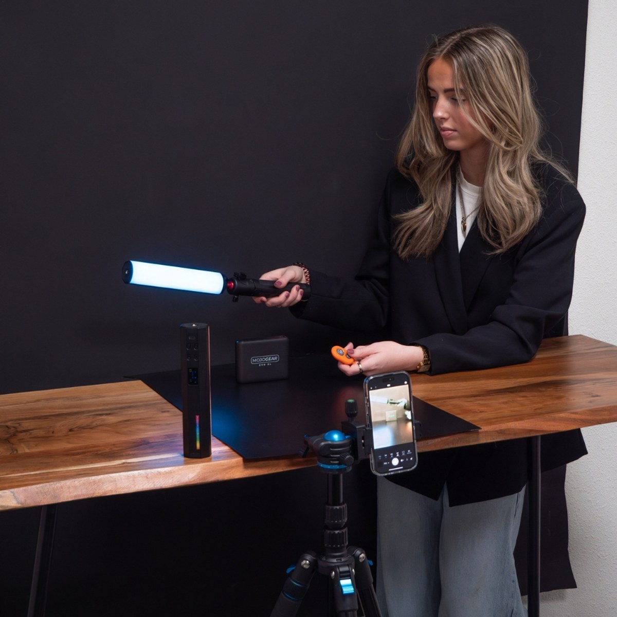 Woman holding a blue light wand at a wooden desk with a smartphone on a tripod.