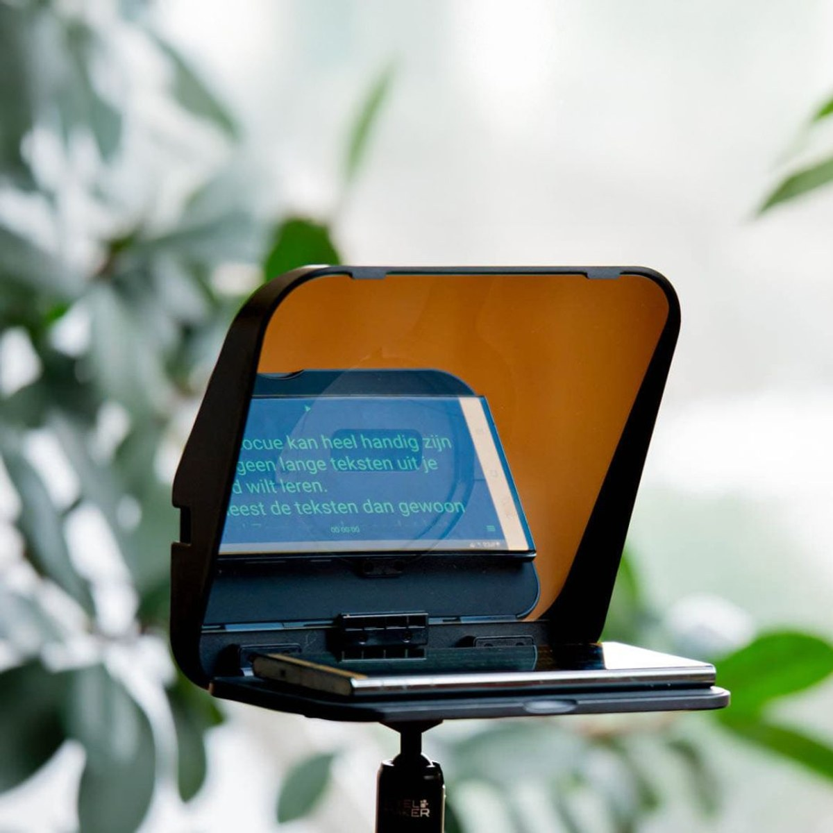 Un smartphone sur un petit trépied avec un prompteur reflétant du texte vert, sur un fond vert flou.