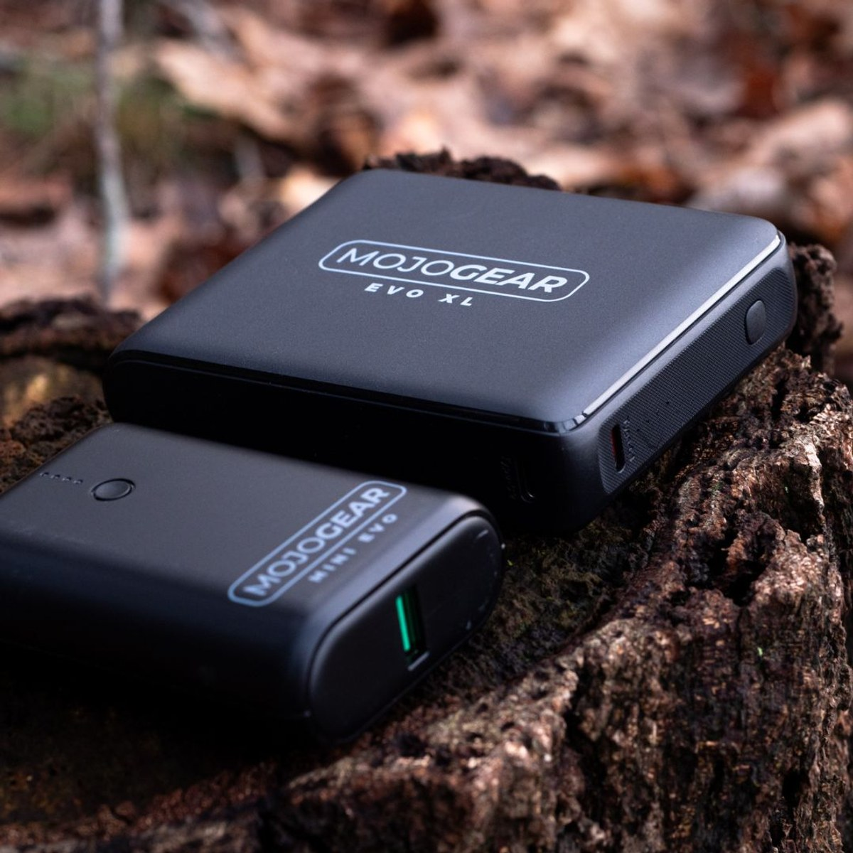 Deux batteries externes noires Mojogear posées sur une souche d'arbre en extérieur.