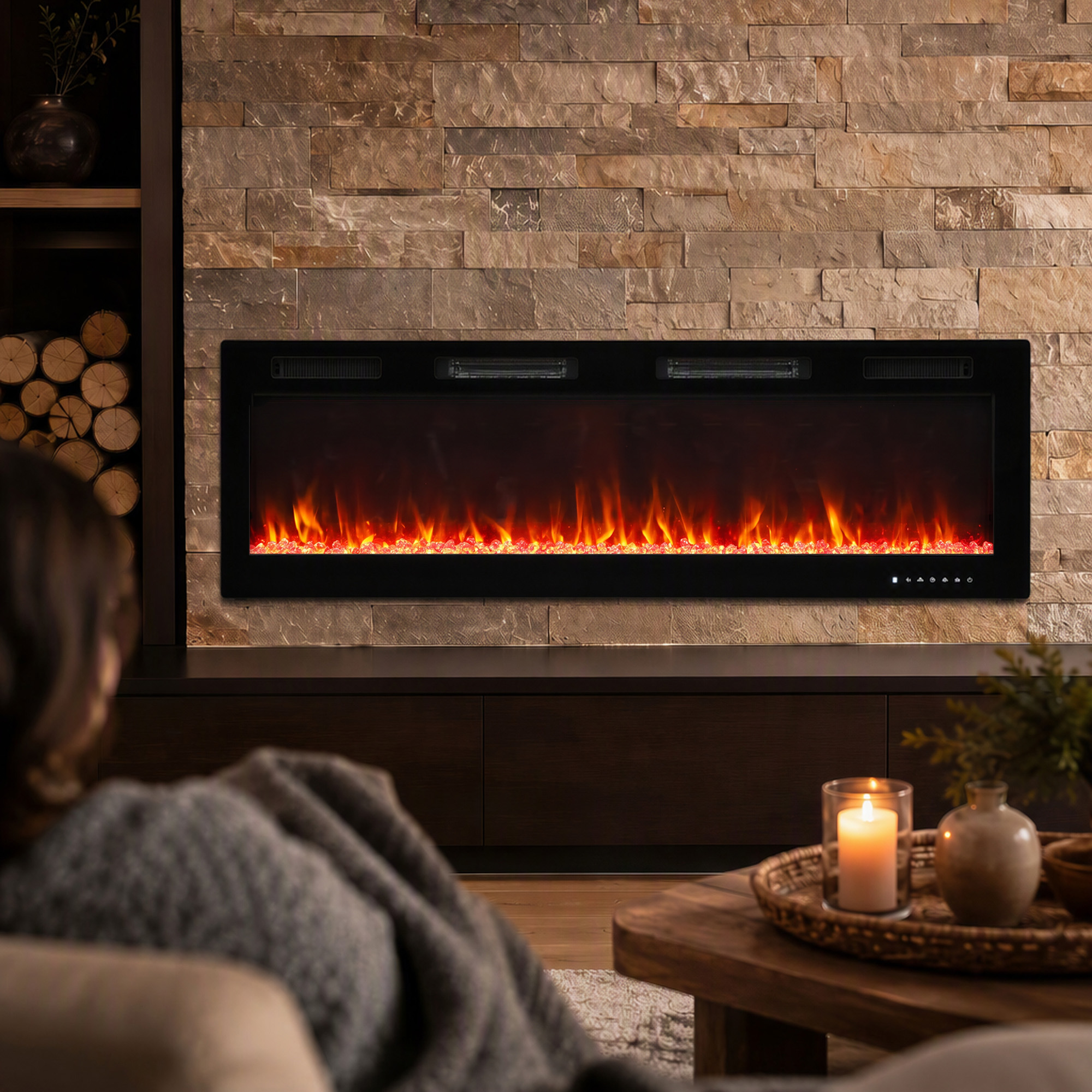 Persona con coperta davanti a caminetto elettrico su parete di pietra, con tavolo e candela.