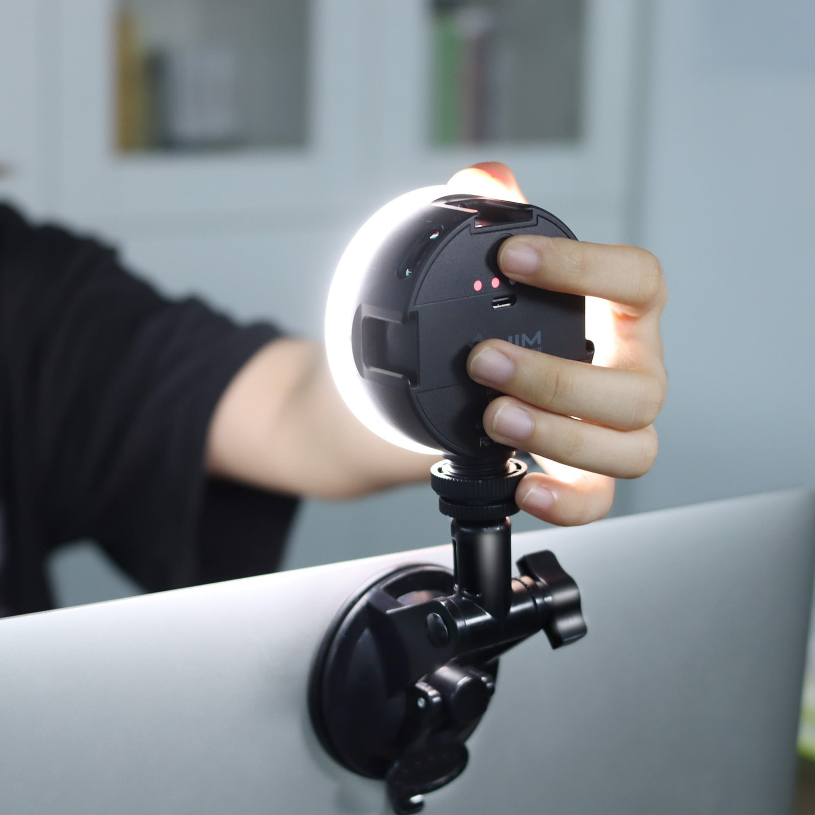 A hand holds a small, glowing ring light attached to a laptop.