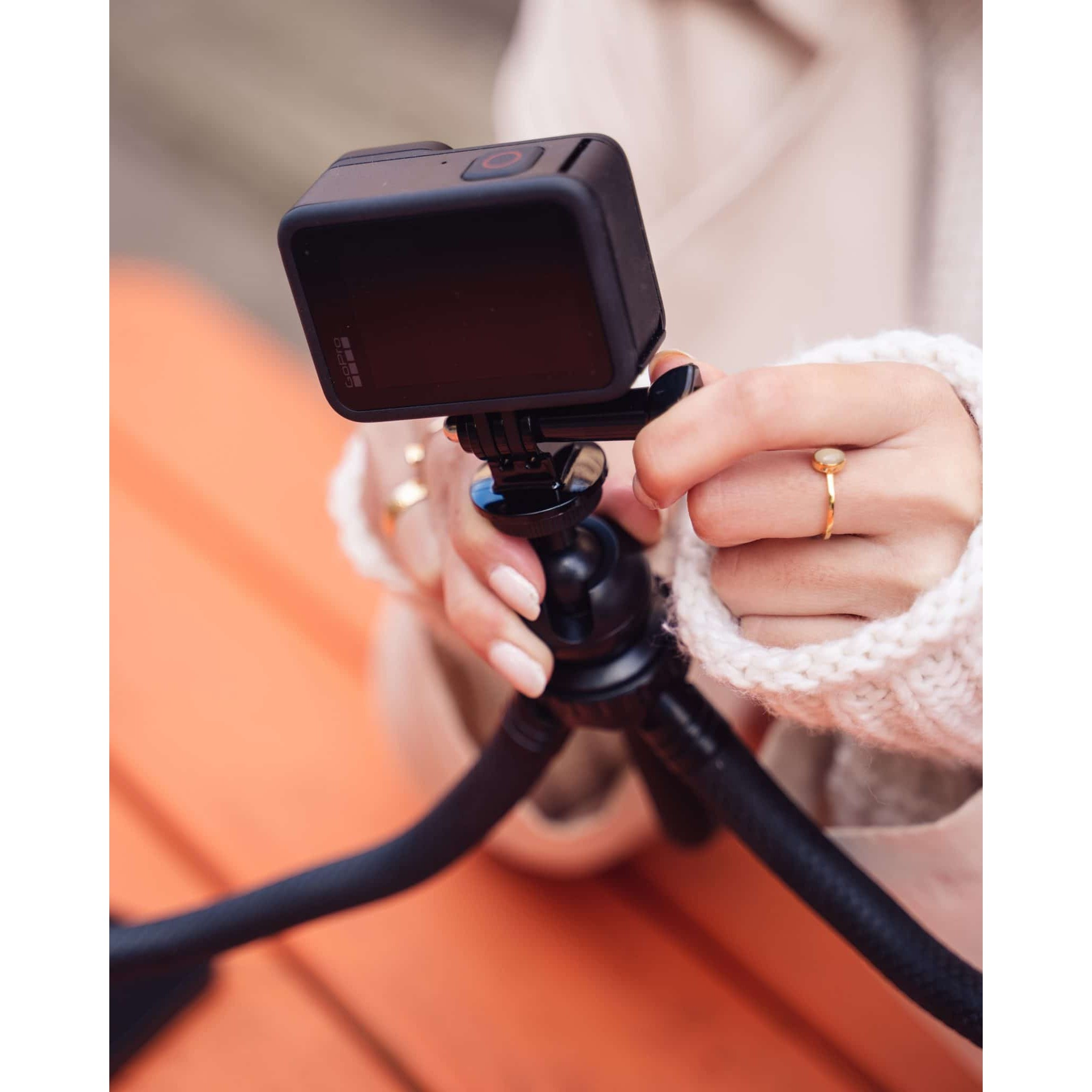A person in a cream-colored sweater adjusts a black action camera mounted on a flexible tripod.