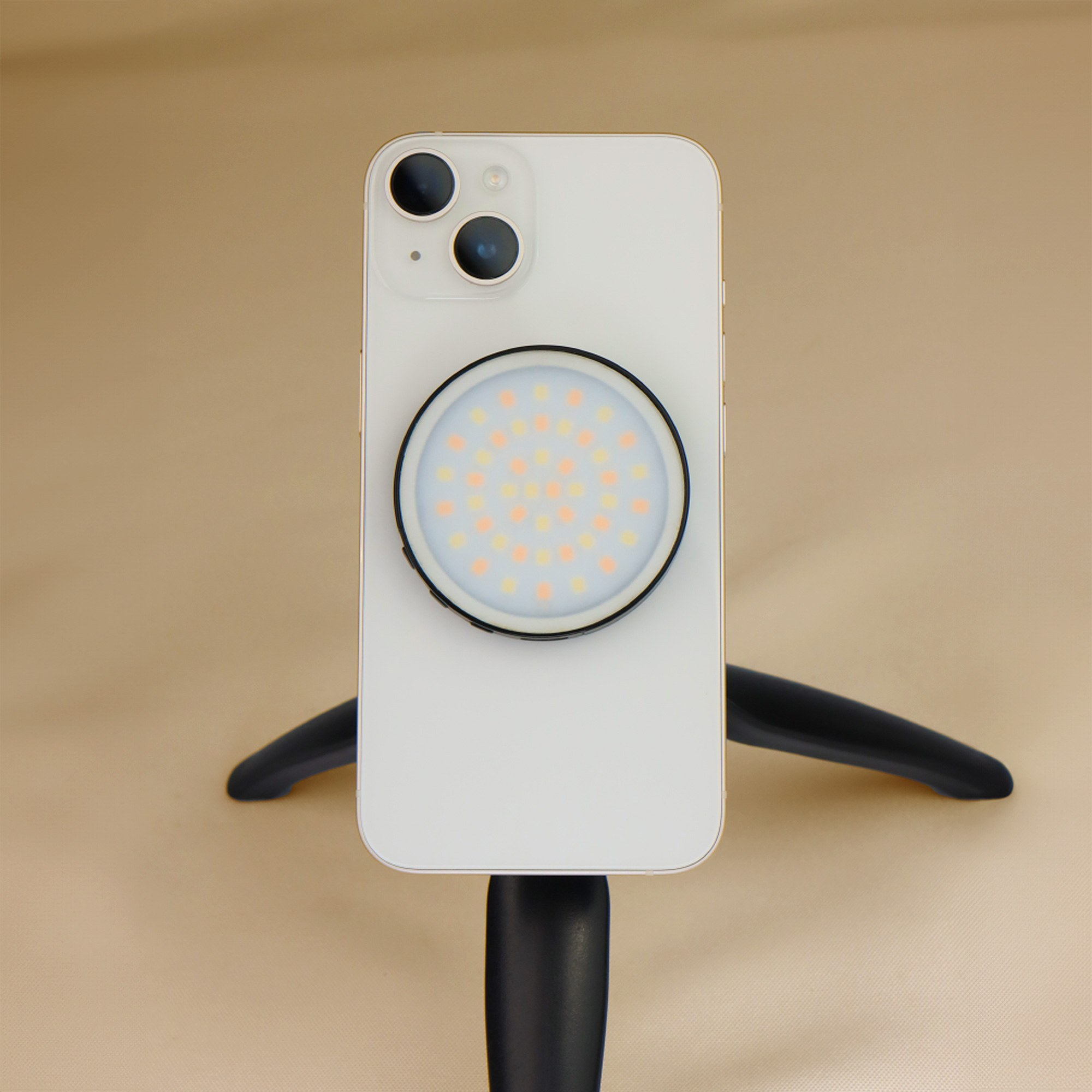 A white smartphone on a black tripod has a round ring light attached to its back.