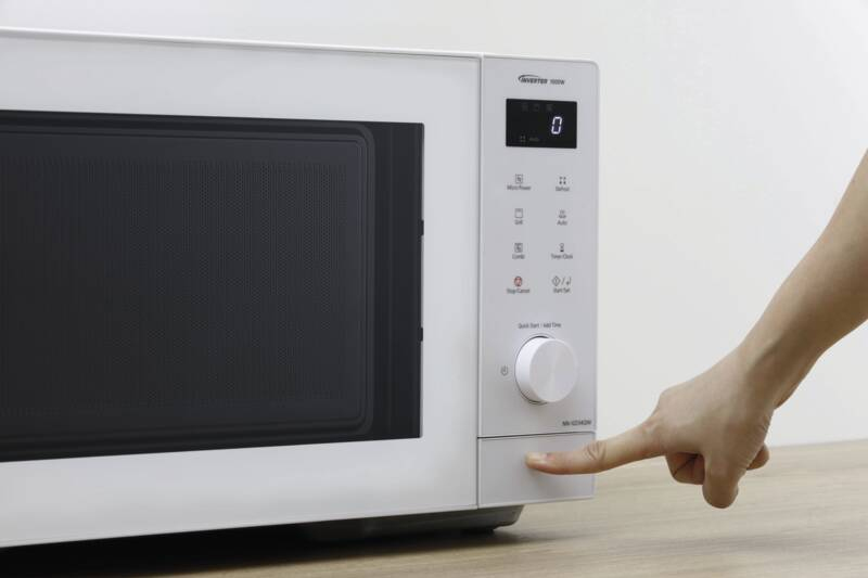 Ręka naciskająca przycisk białej kuchenki mikrofalowej na stole.