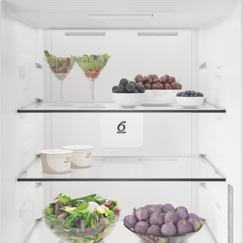 Biała lodówka z półkami wypełnionymi świeżą sałatką, jagodami, wiśniami i figami.